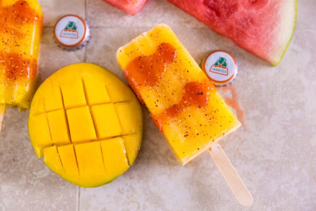 Close-up of Mango Ice Candy in a clear plastic bag with slices of fresh ripe mangoes and a splash of milk in the backgro