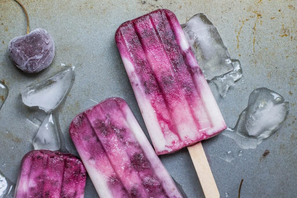 Close-up of Ube Ice Candy in a clear plastic bag with chunks of cooked purple yam ube and a drizzle of condensed milk in