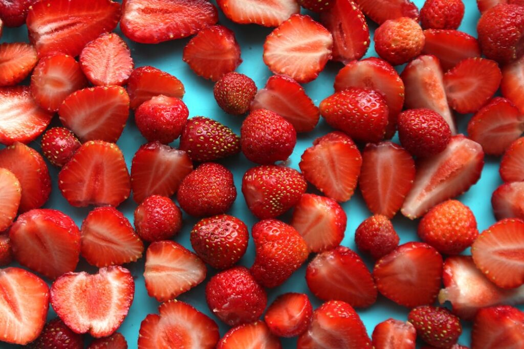 Close-up of pink Strawberry Ice Candy in a clear plastic bag with fresh whole and sliced strawberries and a hint of crea