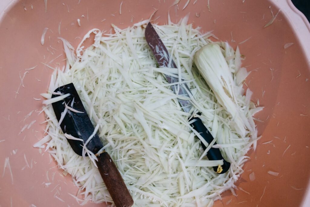 A close-up of a small blender with grated potato and cooked rice inside with a hand pouring in a small amount of water