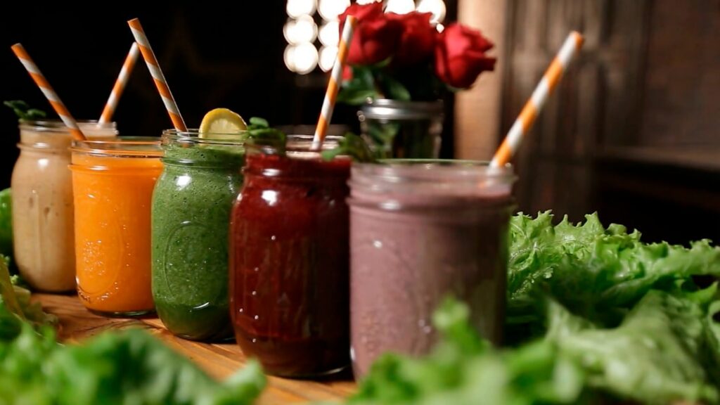 A vibrant healthy beverage possibly a red or orange smoothie or infused water in a clear glass surrounded by fresh ingre