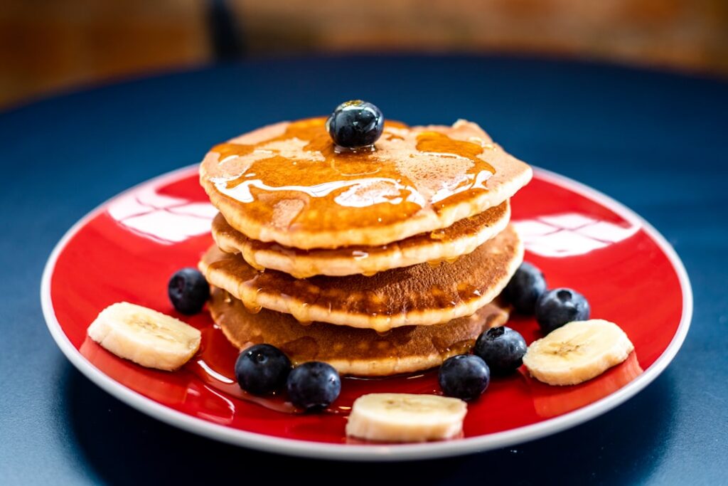 A stack of fluffy golden oat pancakes with fresh berries and a light drizzle of maple syrup set in a cozy breakfast scen
