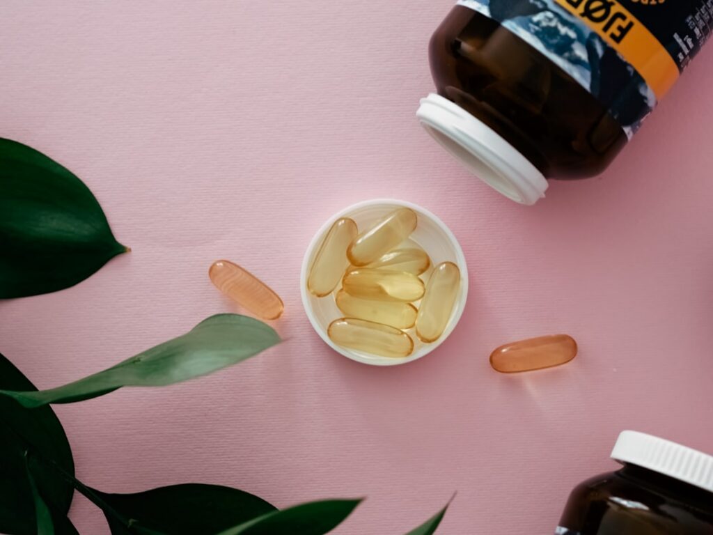 A hand squeezing oil from a golden vitamin E capsule into a bowl with Vaseline