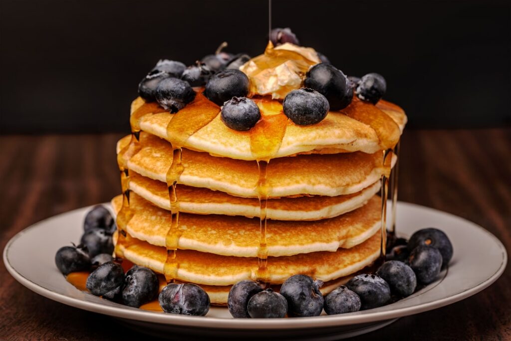 A stack of fluffy blueberry pancakes topped with fresh blueberries and a light drizzle of syrup in a bright morning sett