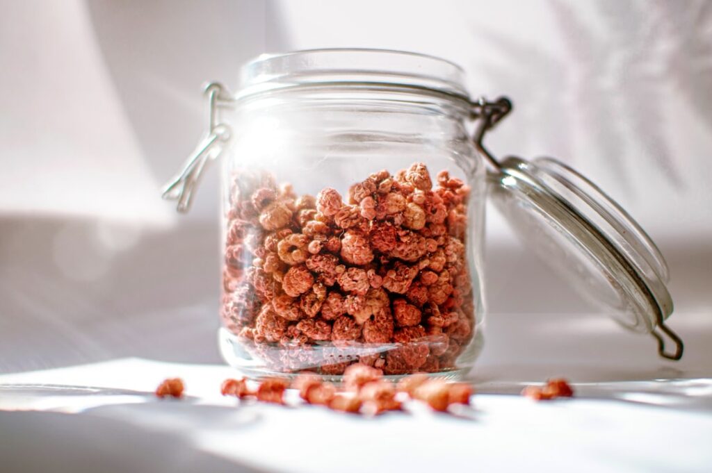 Dried whole cloves being placed into a clear glass jar ready for oil infusion