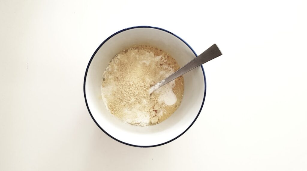 A beautiful close-up shot of a bowl filled with a fine light brown herbal powder with some dried rose petals and turmeri