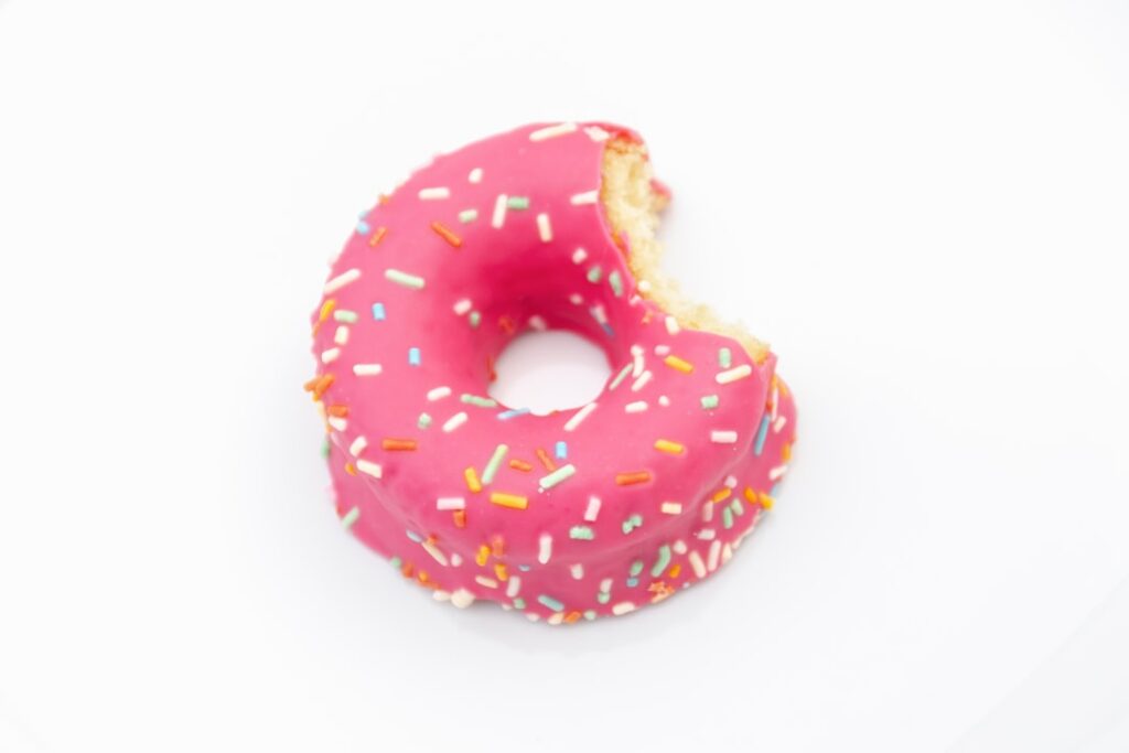 A homemade donut with a vibrant pink strawberry glaze and colorful sprinkles on a white plate