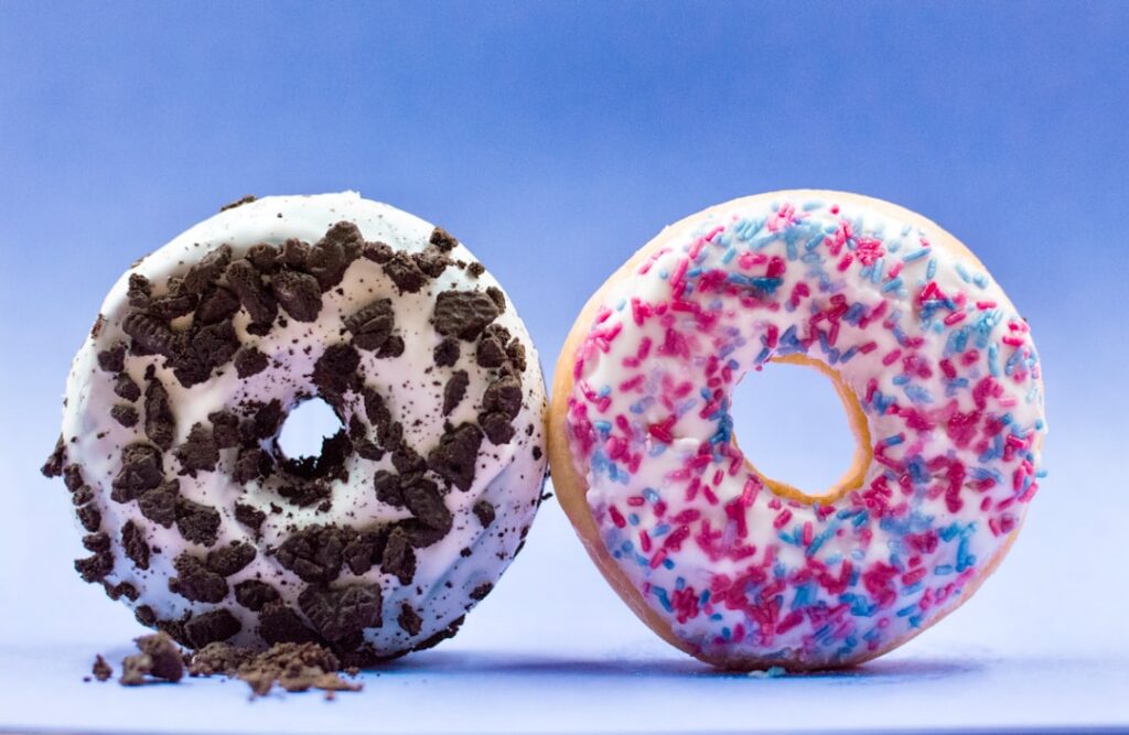 A homemade donut with white cream cheese frosting and generous crushed chocolate cookies on top on a white plate