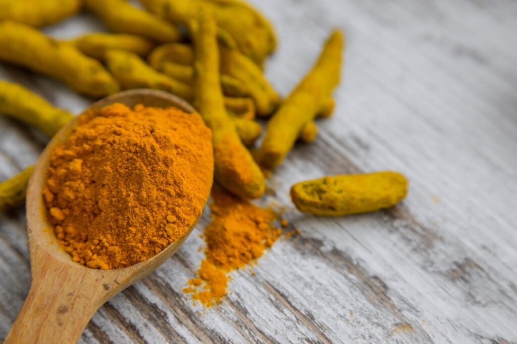 A vibrant golden turmeric drink in a glass with fresh turmeric roots and slices of lemon and ginger next to it on a rust