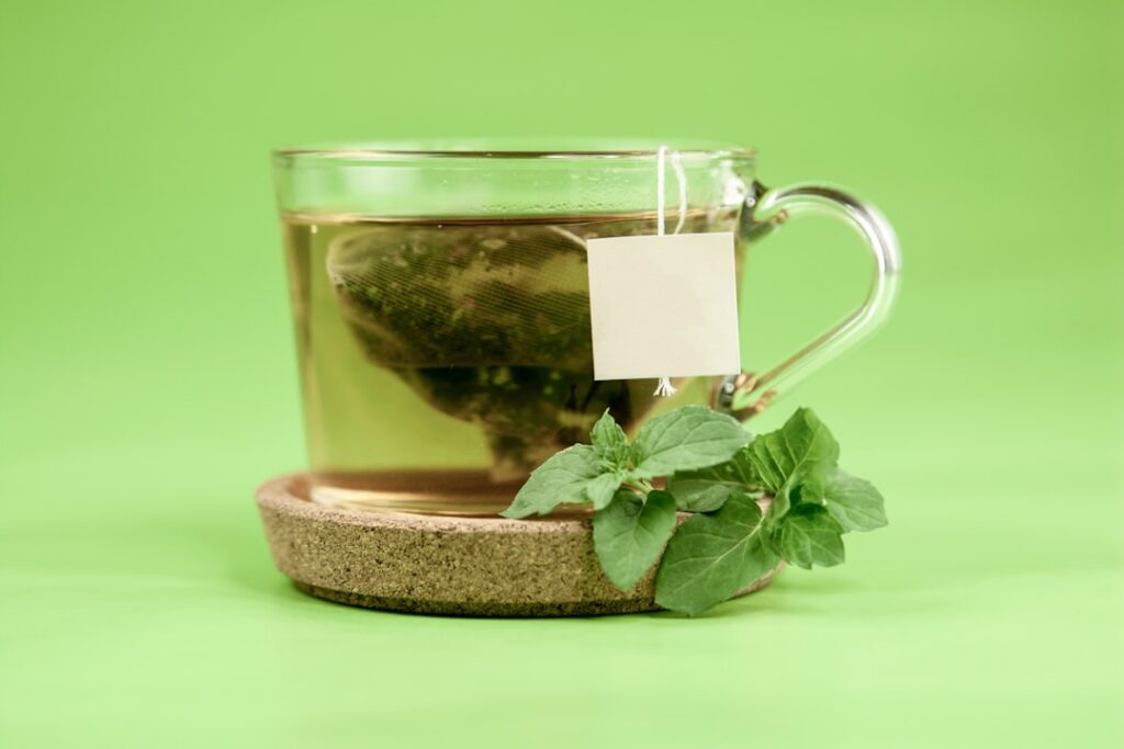 A warm cup of Asthma Weed tea steeping with steam rising a timer next to it and some dried herb in a small bowl