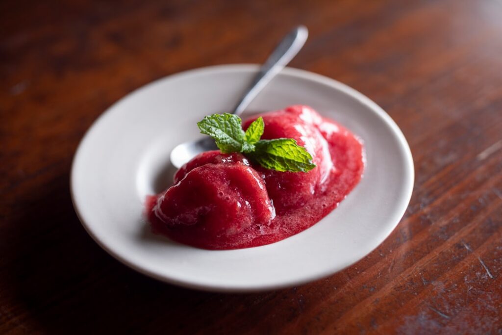A vibrant refreshing bowl of homemade berry sorbet garnished with fresh mixed berries like strawberries blueberries and 