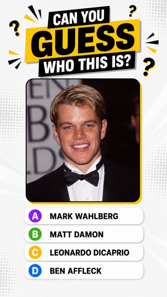 Young Matt Damon in a black tuxedo at an awards event smiling at the camera The background is blurred with hints of Gold