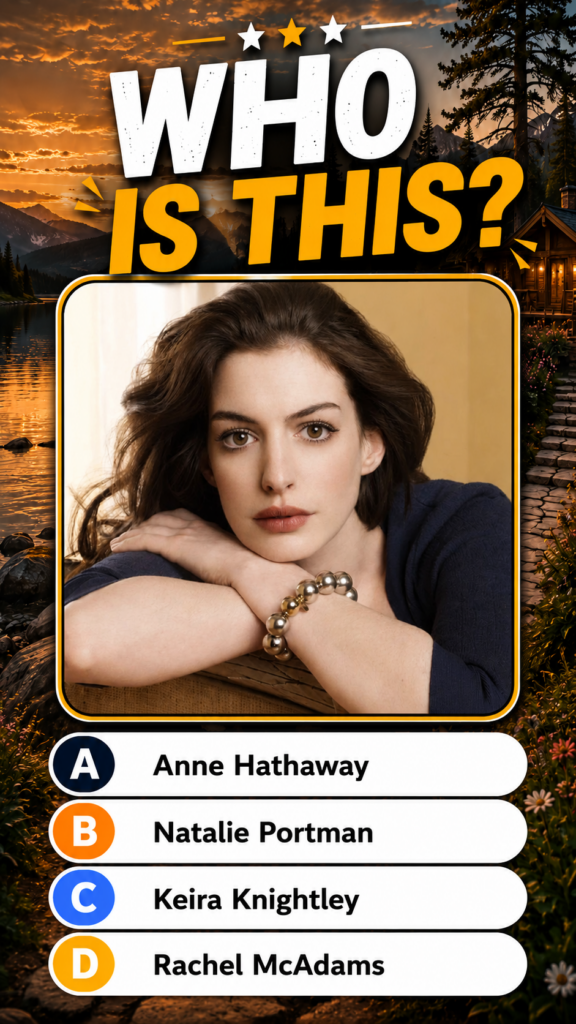 A portrait of a young Anne Hathaway with a contemplative expression resting her chin on clasped hands wearing a dark blu