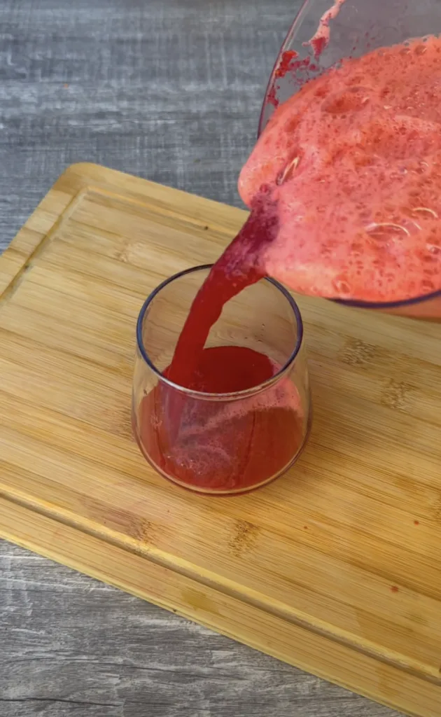 Vibrant red foamy liquid being poured from a blender into a clear glass