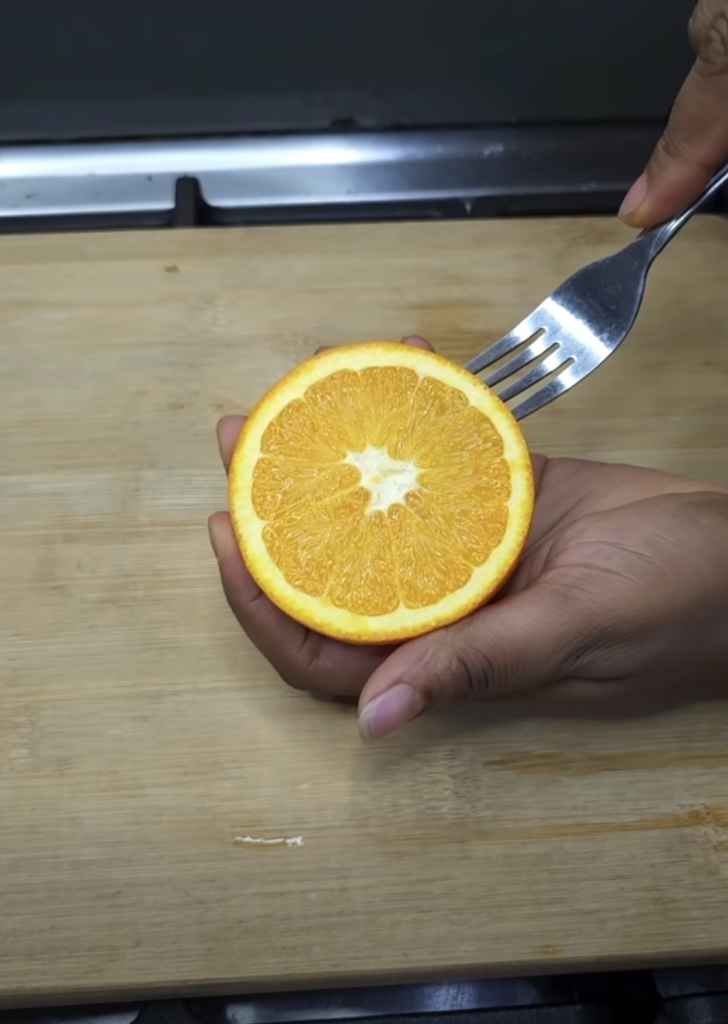 Close-up of hands holding a perfectly halved vibrant orange with a fork resting on a warm-toned wooden cutting board