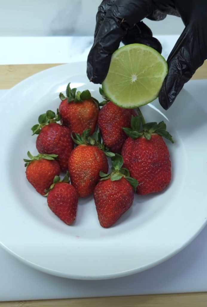 A close-up overhead shot of a white plate filled with fresh ripe red strawberries with a hand gloved in black holding a 