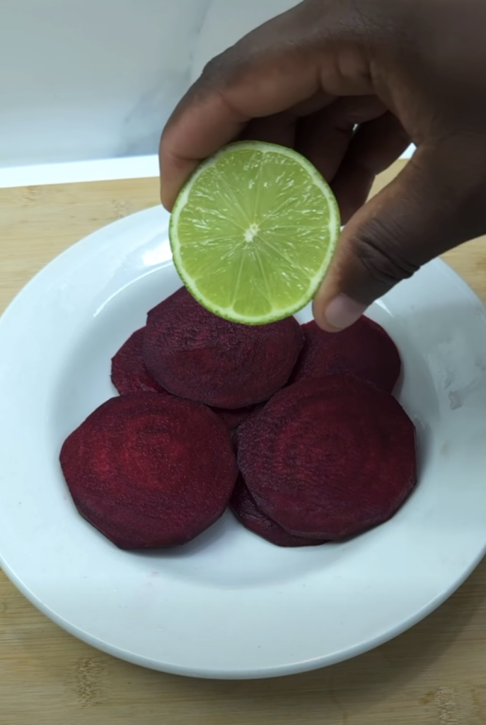 A hand squeezing a vibrant green lime half over deep red beetroot slices on a white plate