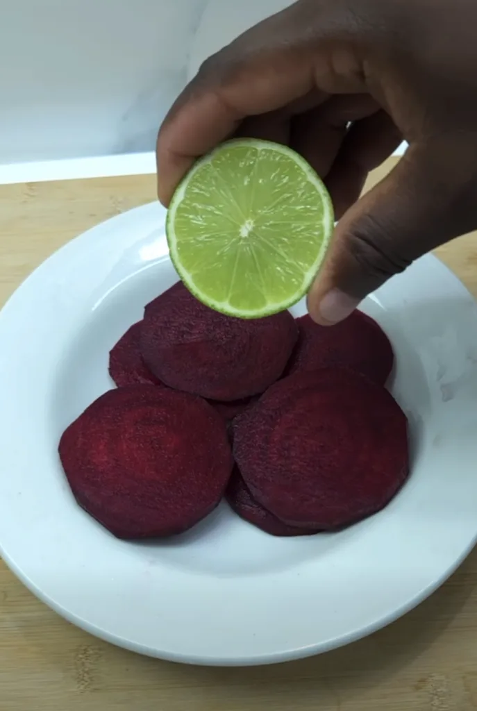 A hand squeezing a vibrant green lime half over deep red beetroot slices on a white plate