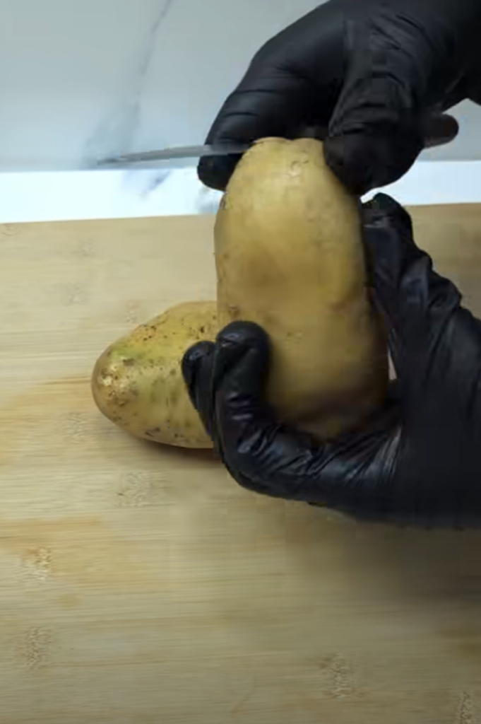 Hands peeling a potato on a wooden cutting board