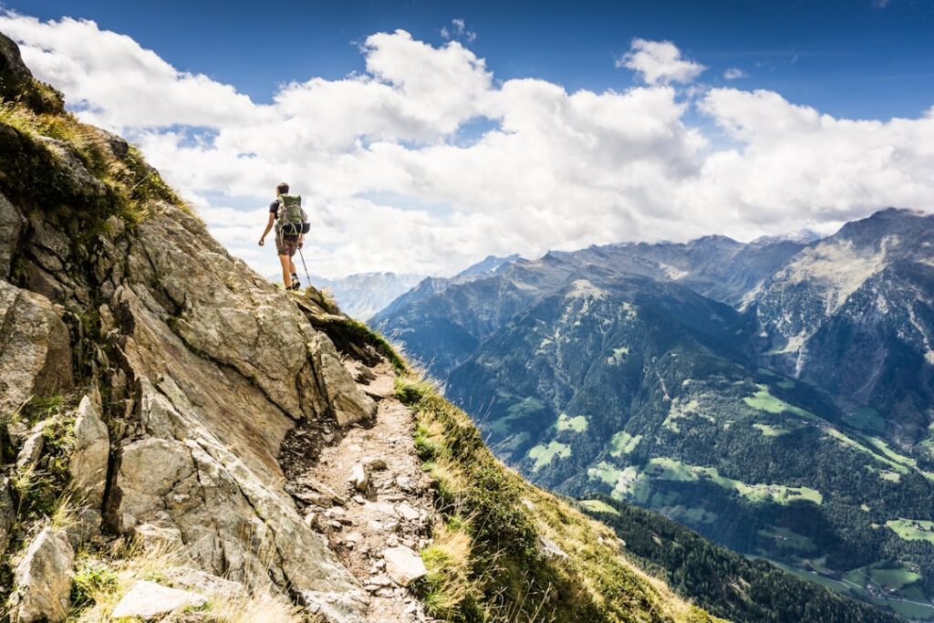 A person hiking uphill on a scenic trail with mountains in the background