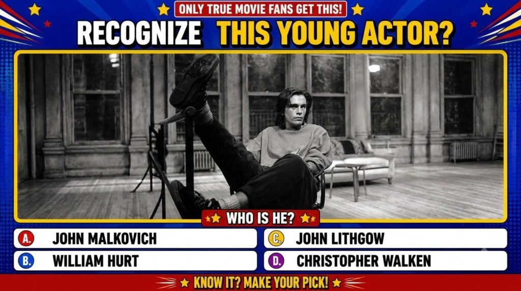 A black and white photograph of a young John Malkovich seated casually on a chair with one leg propped up looking though