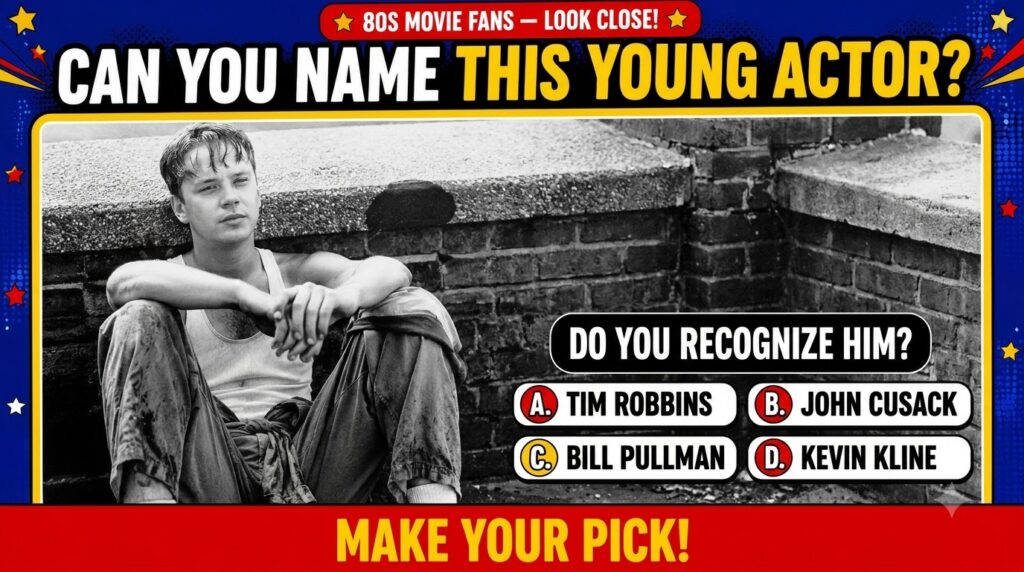 A black and white photograph of a young Tim Robbins in a tank top and loose pants sitting against a concrete and brick b