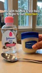 A small clear glass jar filled with a glossy translucent balm with a tub of Vaseline and a bottle of baby oil in the bac