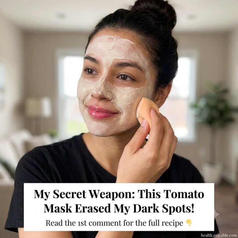 A woman applying a light-colored face mask to her face with a peachy-orange sponge smiling slightly Her hair is pulled b