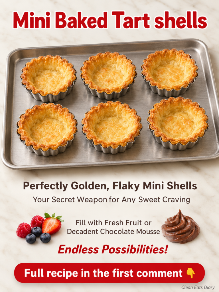 A stainless steel baking tray with several golden flaky mini tart shells resting in their metal fluted molds on a light 