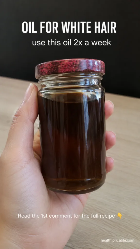 A hand holding a clear glass jar filled with dark hair oil with text overlays OIL FOR WHITE HAIR and use this oil 2x a w