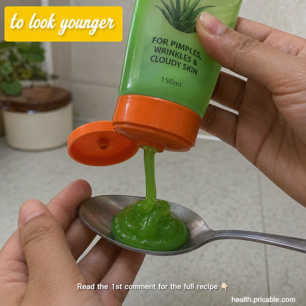 A hand squeezing bright green gel from a tube onto a metal spoon with an aloe vera plant graphic on the tube in a home s