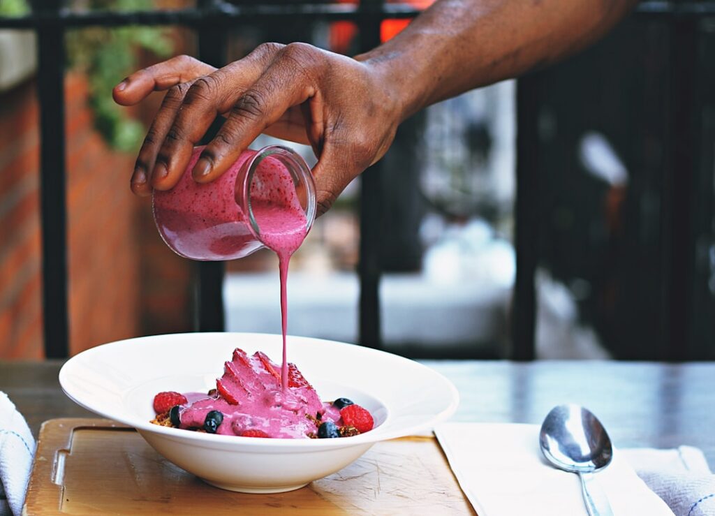 A close-up shot of a healthy breakfast smoothie being poured into a tall glass garnished with fresh berries and a sprink