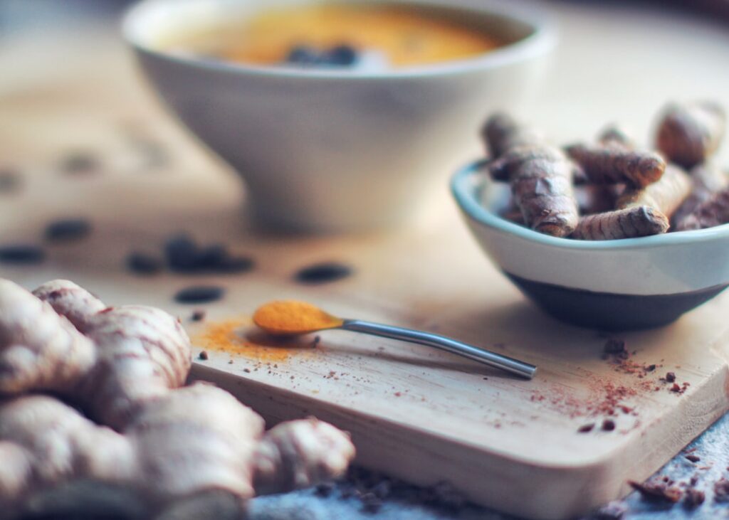 Close-up of fresh ginger root green cardamom pods and a small bowl of ground turmeric ready for making a beauty drink