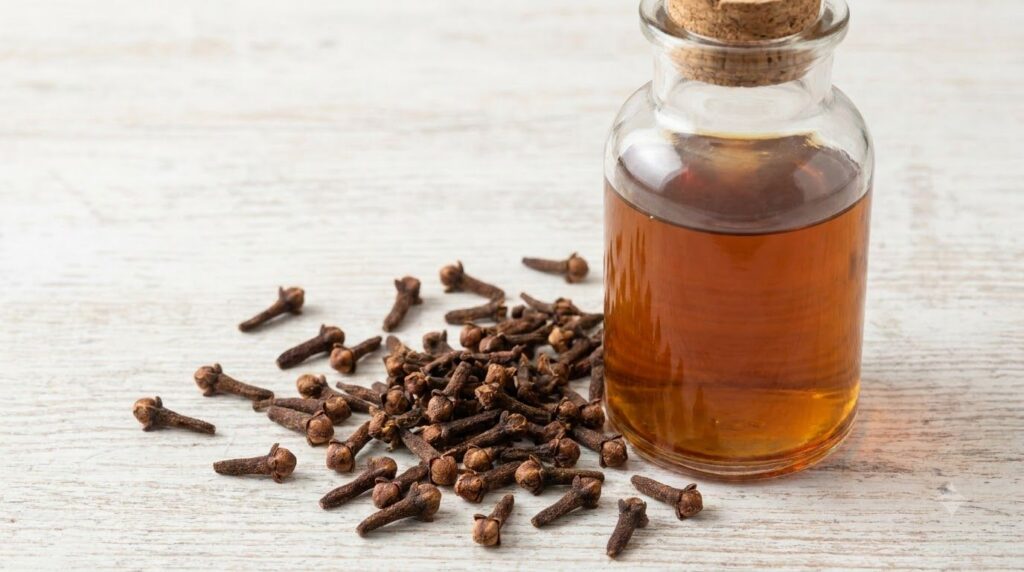 Small dried whole cloves scattered on a light surface with a glass bottle containing a clove-infused liquid representing