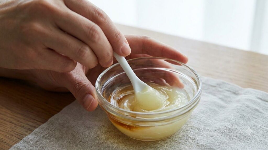 Close-up of a person mixing Vaseline and Vitamin E oil in a small bowl with a spatula