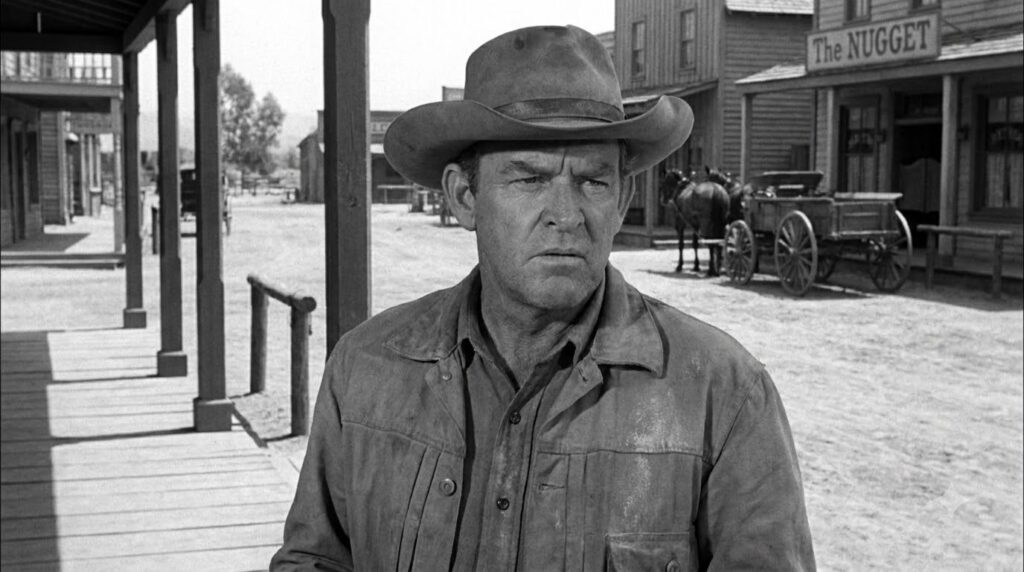 Denver Pyle in a black and white still from an old Western film or TV show wearing a cowboy hat and a serious expression