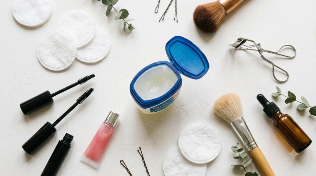 Various everyday beauty items arranged around a jar of Vaseline illustrating its versatility such as cotton pads a small