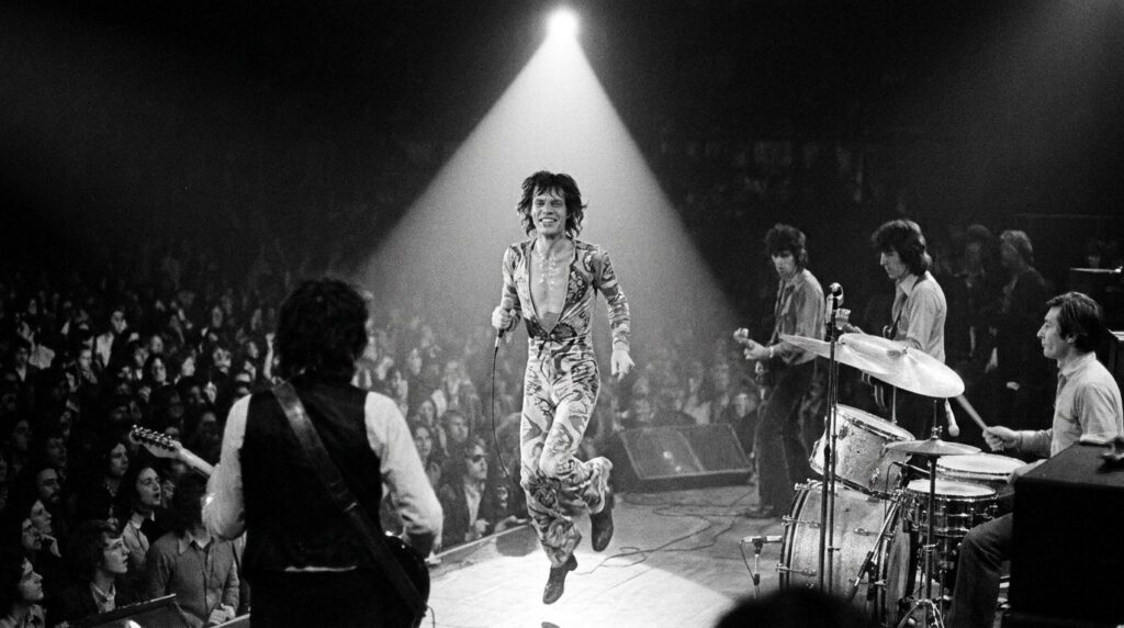 A real archival photo of Mick Jagger performing on stage with The Rolling Stones in the 1970s showcasing his energetic s