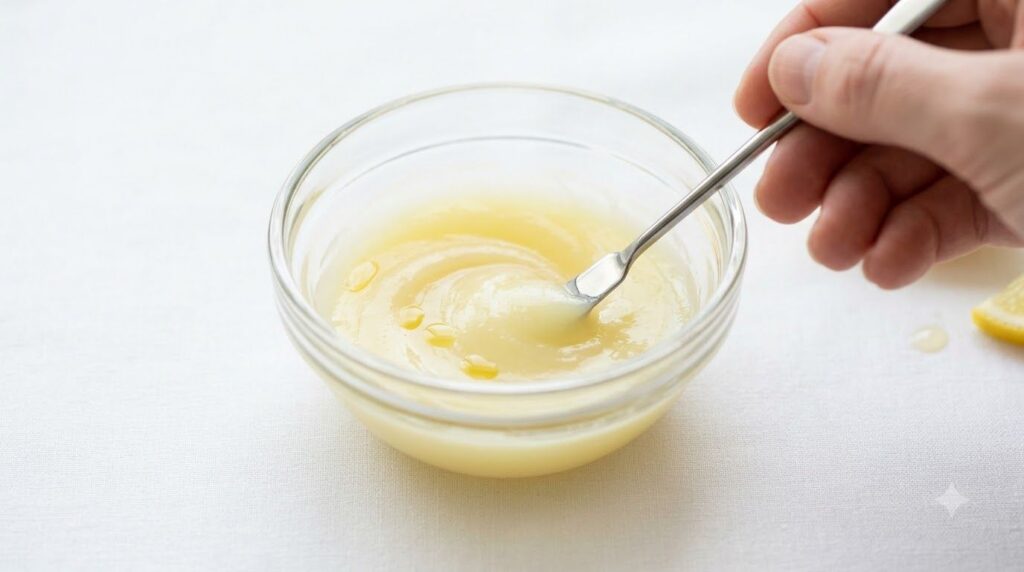 Close-up of a small glass bowl with Vaseline baby oil and lemon juice being stirred together with a mini spatula creatin