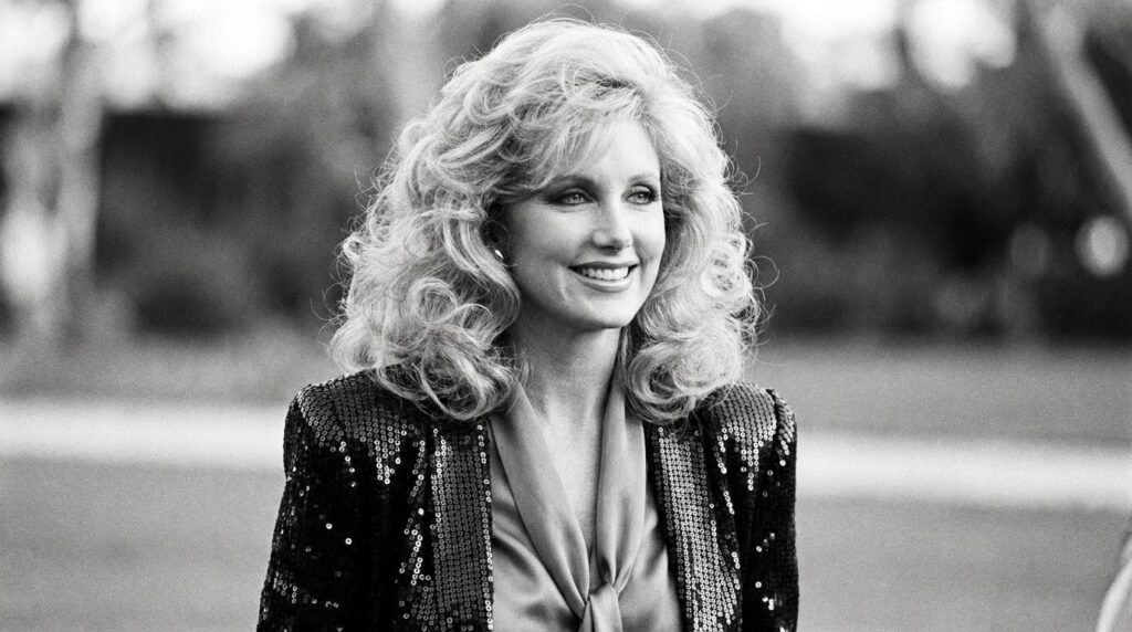 Real archival photo of Morgan Fairchild showcasing her signature voluminous blonde hairstyle and glamorous fashion from