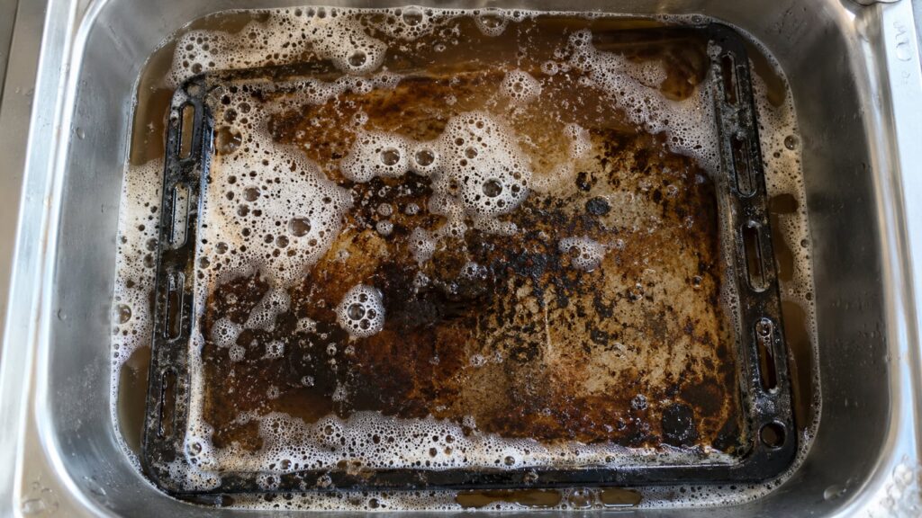 Una bandeja de horno sucia sumergida en una solución espumosa de cola y jabón en un fregadero