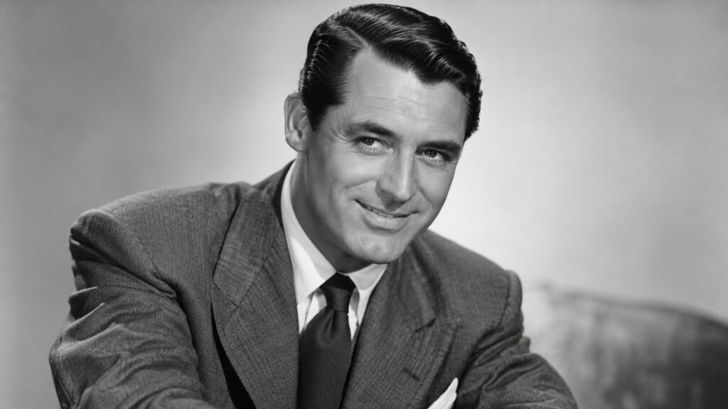 A classic black and white publicity photo of Cary Grant smiling with his characteristic charm
