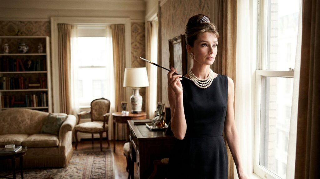 Audrey Hepburn as Holly Golightly in Breakfast at Tiffany s wearing a black dress pearls and a tiara holding a cigarette