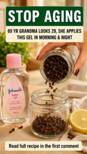 A small clear glass bottle filled with a golden infused oil surrounded by whole cloves fresh lemon zest and a bottle of 