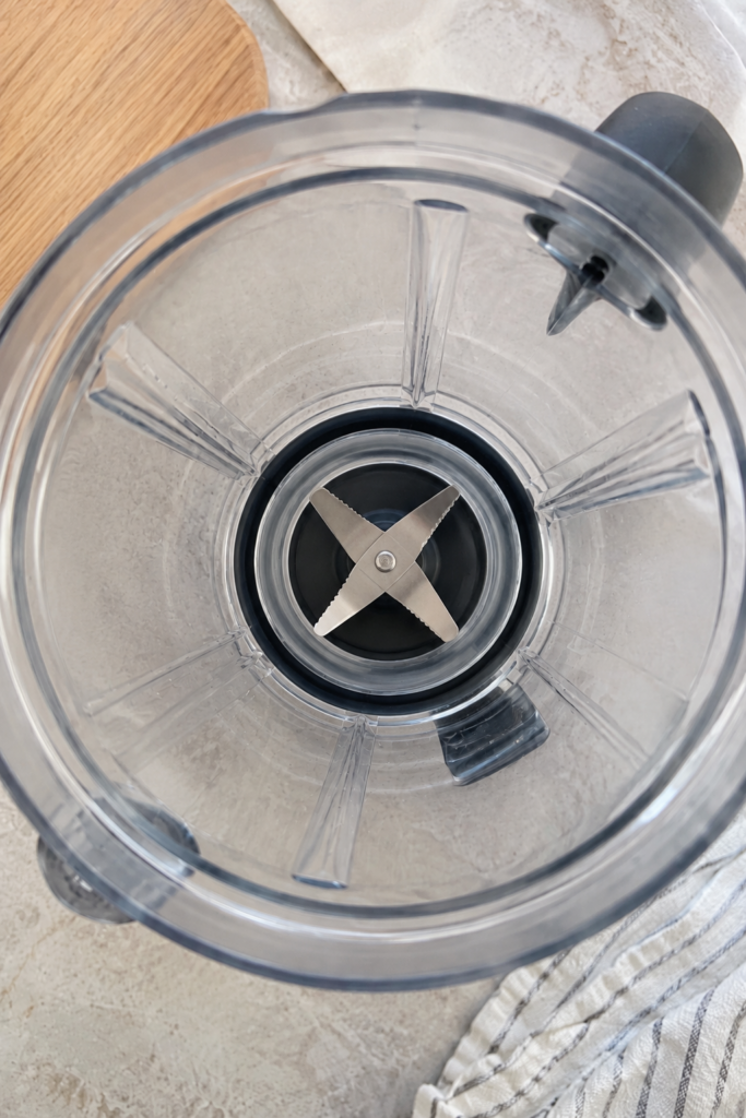 A top-down inside view of an empty clean blender jar featuring the metallic four-pronged blade assembly at its center Th
