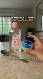 A small elegant jar of the finished Vaseline and baby oil glass skin balm sits on a vanity next to a bottle of baby oil 
