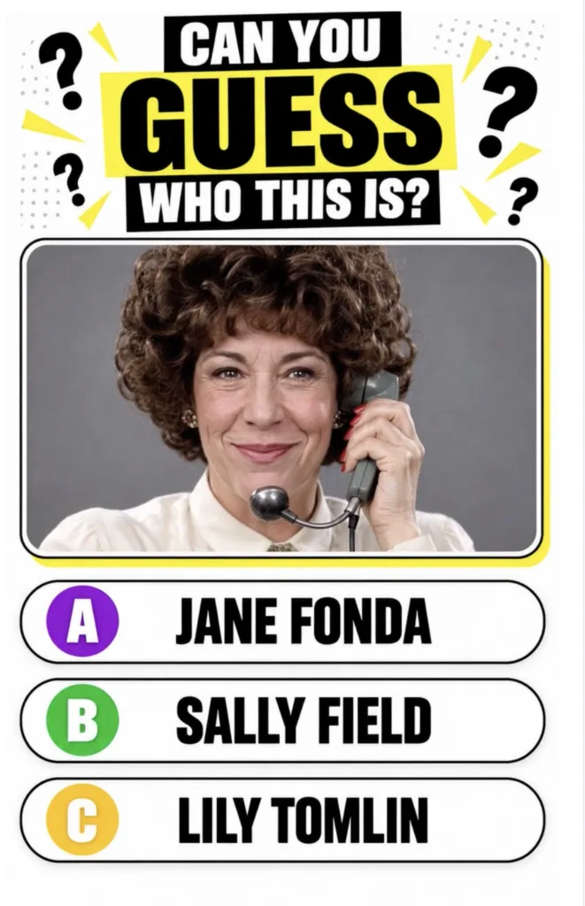 Lily Tomlin as Ernestine holding an old-fashioned telephone receiver with a headset smiling at the camera