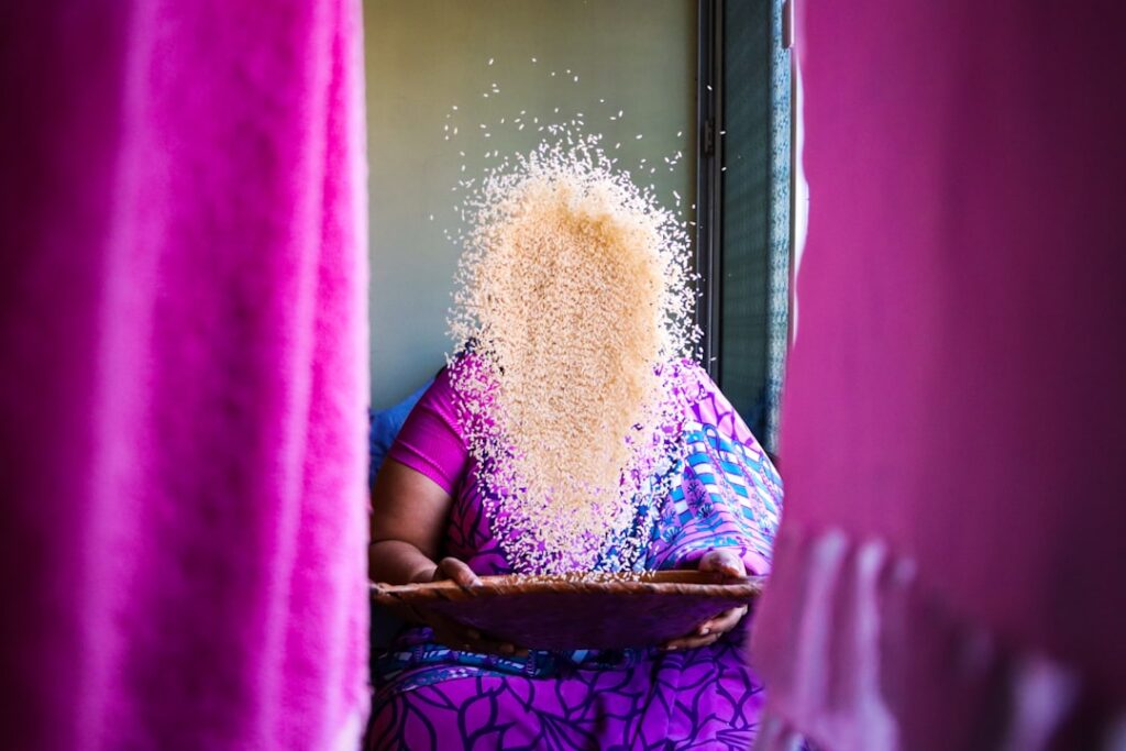 A woman gently pouring rice water over her long dark hair in a shower with steam and soft lighting showing a natural hai