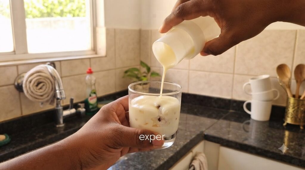 Dark-skinned hands pouring a thick creamy white liquid from a white container into a glass already containing a layered 