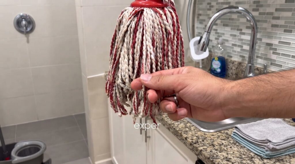 A close-up of a wet mop head with red and white twisted cotton strands a finger gently touching one of the wet strands w
